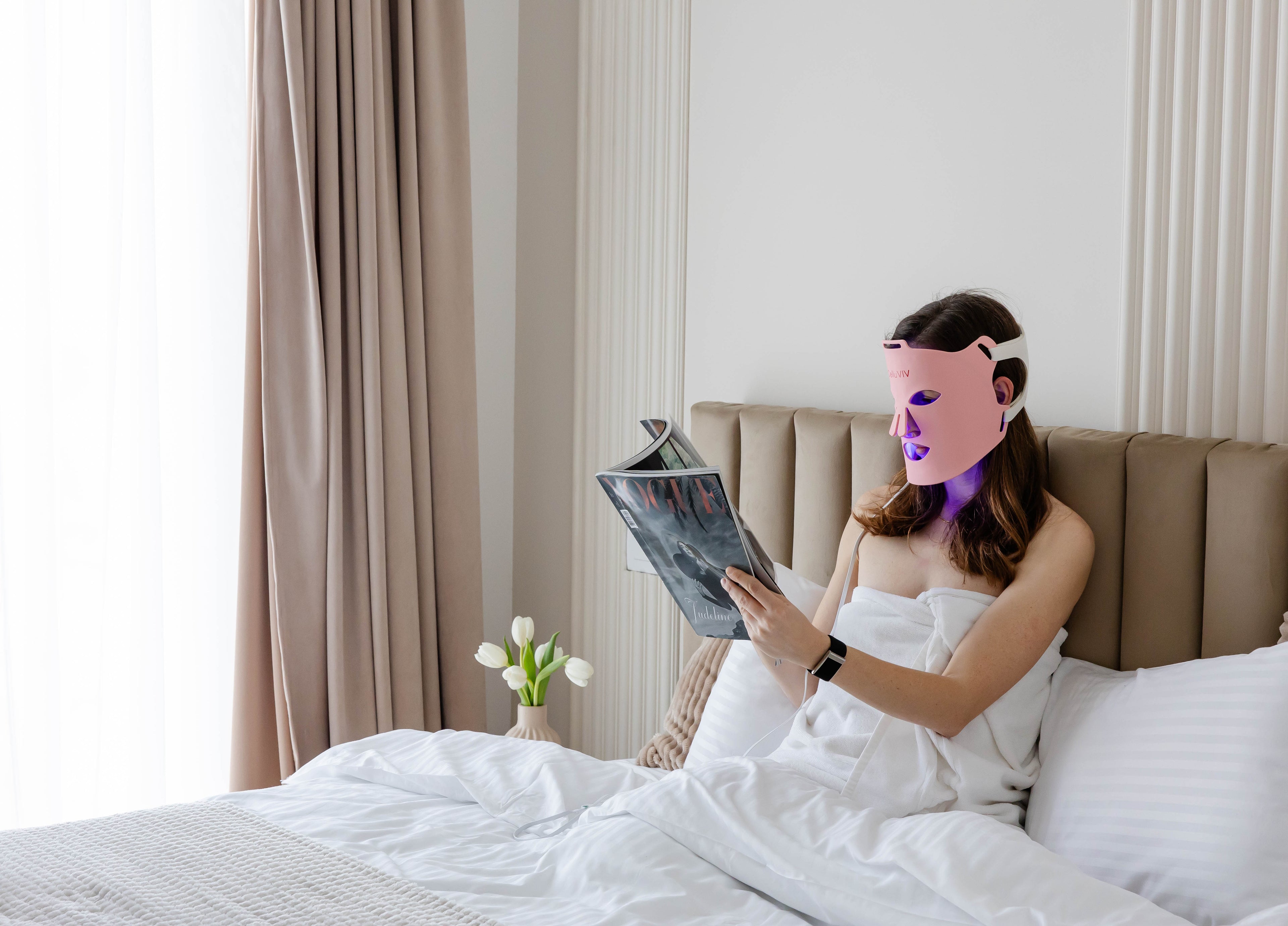 LED face mask used by a women in bed reading a magazine showing easy to implement routine