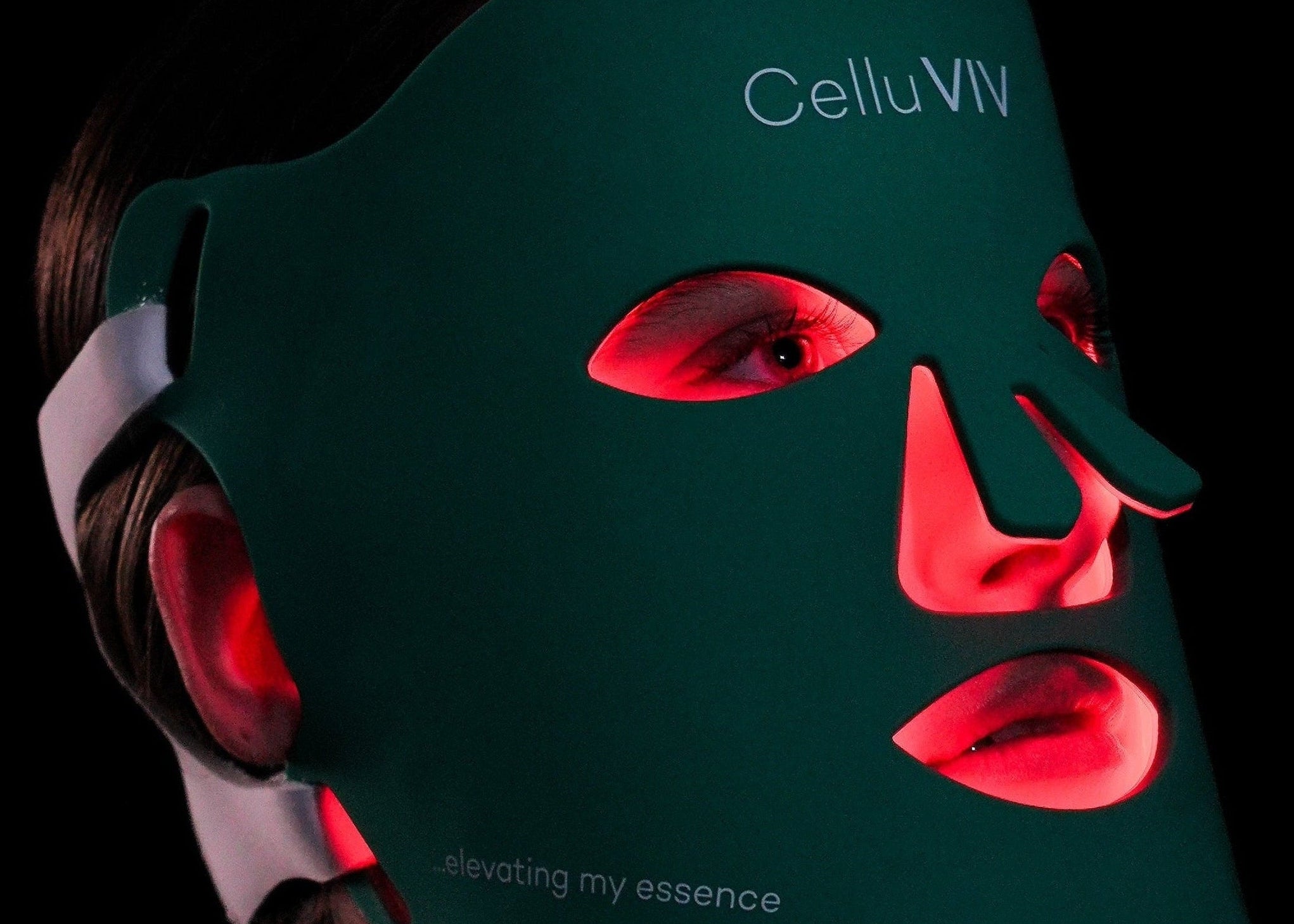 Person wearing a green LED face and neck mask with visible branding on a black background
