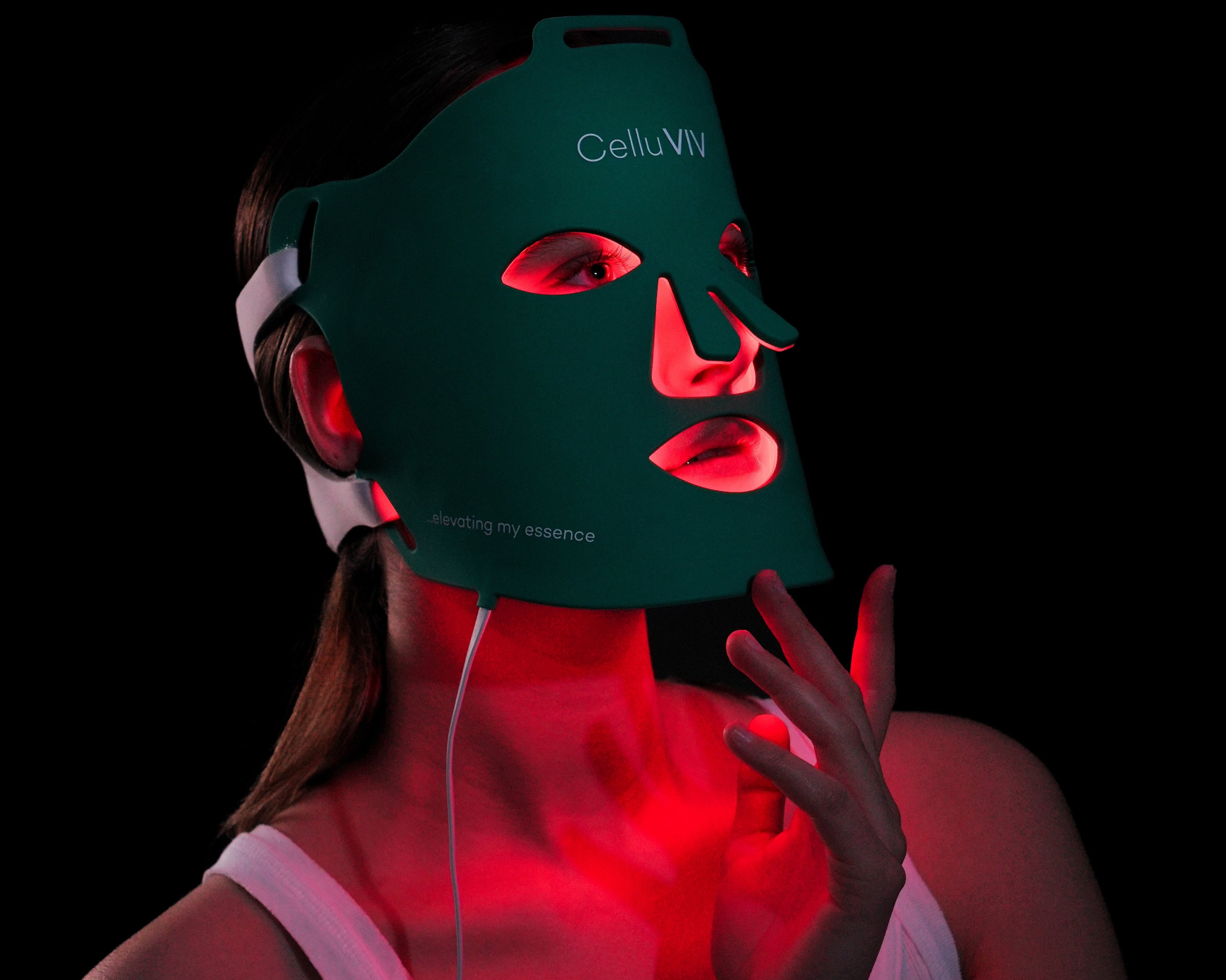Person wearing a green LED face and neck mask with visible branding on a black background